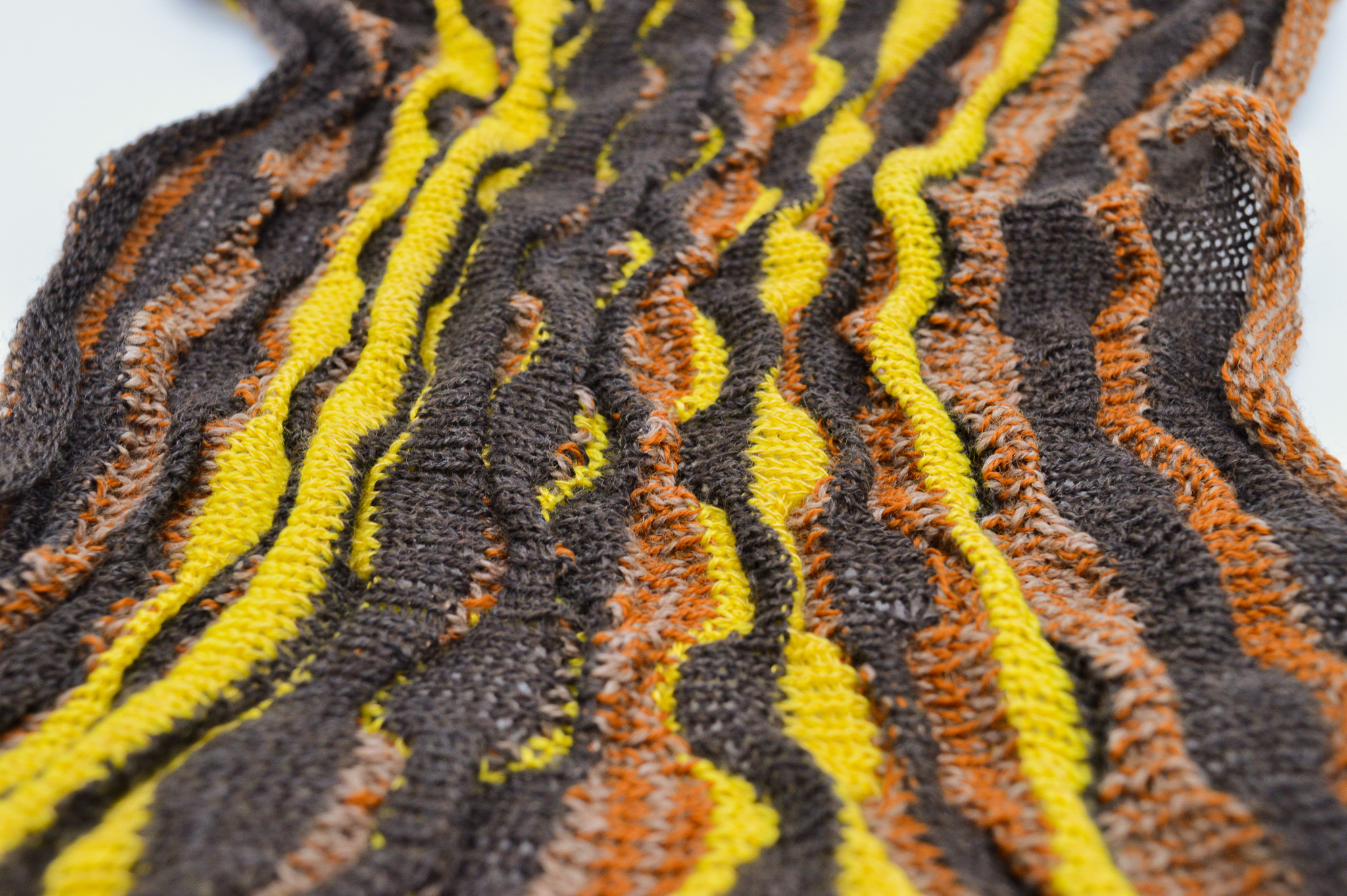 Knit fabric with a pattern of vertical waving stripes in shades of black, yellow and muted browns to form a series of alternating rounded forms.