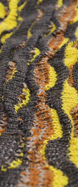 Closeup of a knit fabric whose surface is made up of vertical waves in varying stripes of black, yellow, and browns.