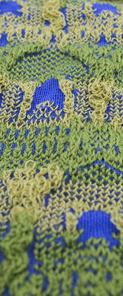 Closeup of a green knit fabric with a pattern of arches which form a raised textured surface interlaced with central blue accents.