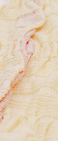 Close-up of a cream knit fabric made up of a series of pleats that create the textured surface with orange accents peeking out from inside the structure.