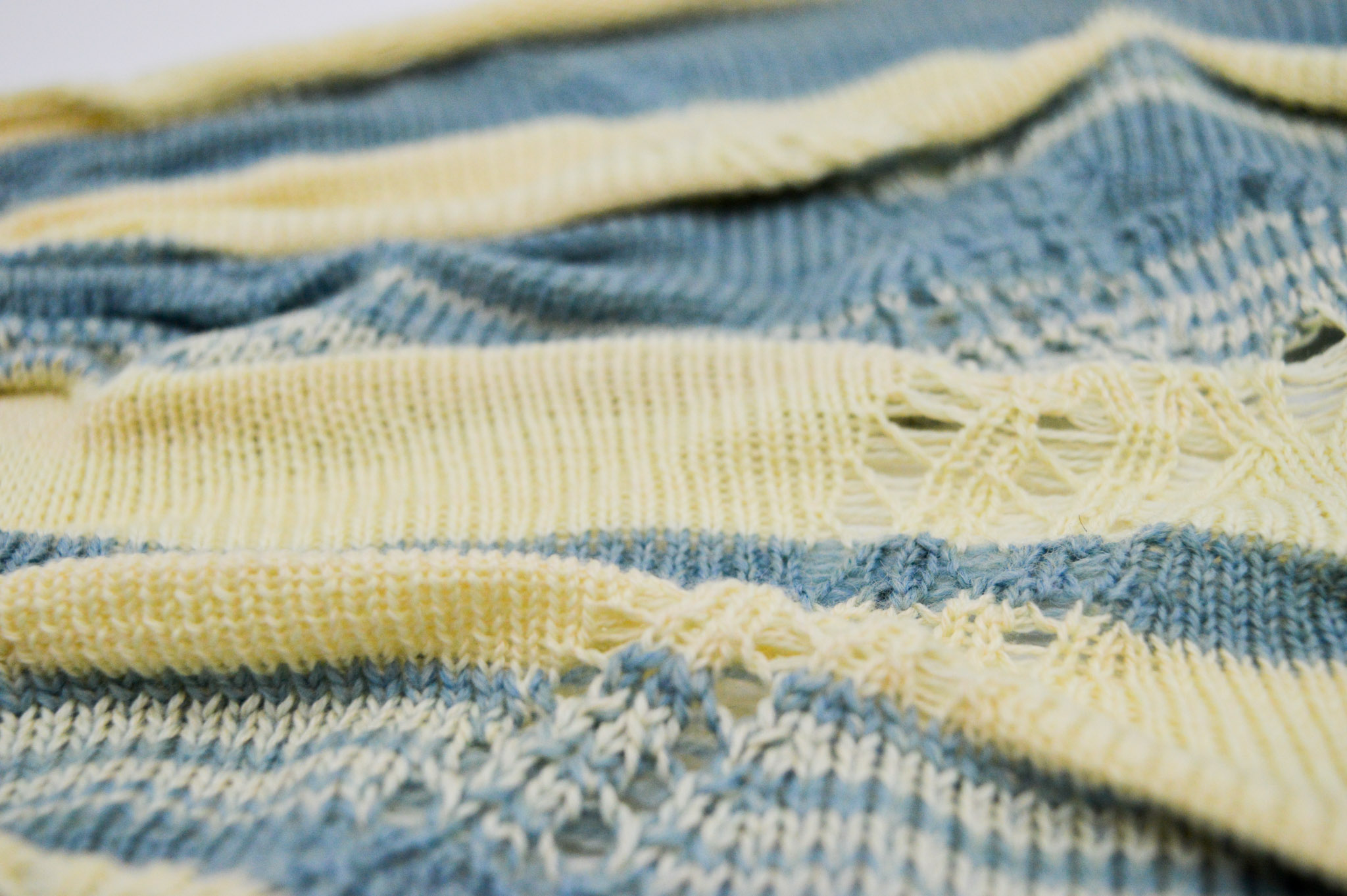 Close-up at an angle of a knit fabric with blue and cream stripes of varying sizes, significant pleating and lacey holes