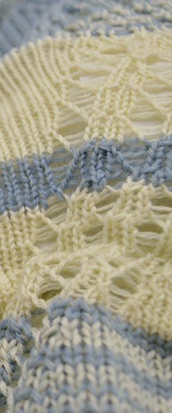 Close-up of a knit fabric with blue and cream stripes and lacey holes accenting the form.