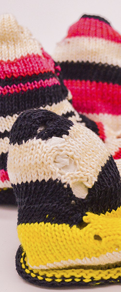 Close-up of a series of knit cones whose surface features large contrasting stripes in black, white, pink and yellow.